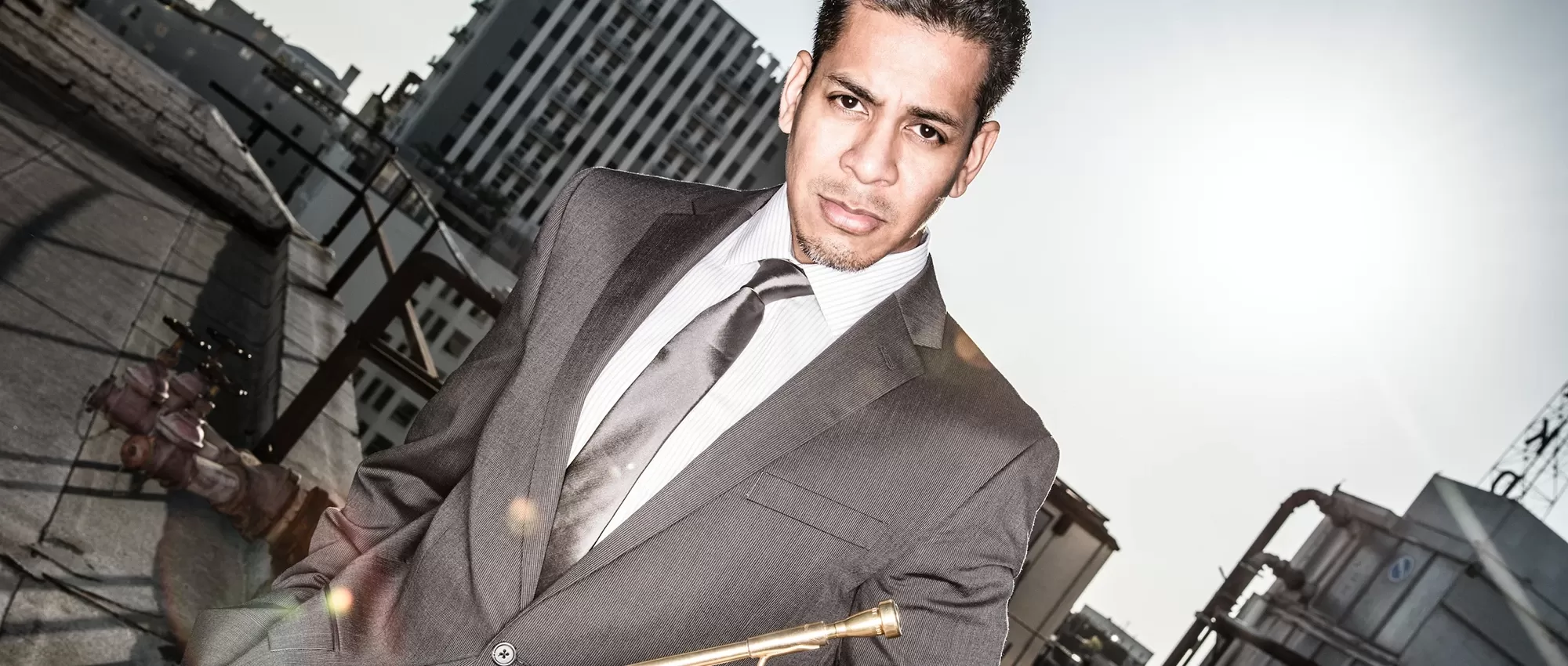 Barry Perkins in a gray suite holding his trumpet in front of a city scene
