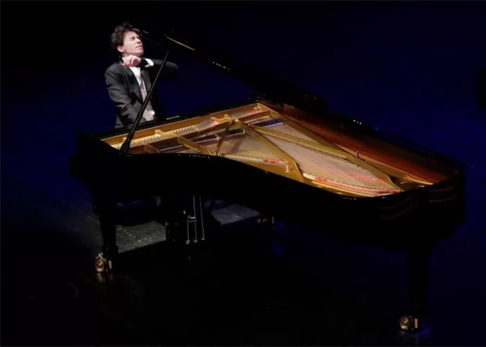 Pianist Angel Stanislav Wang playing a grand piano on a dark stage