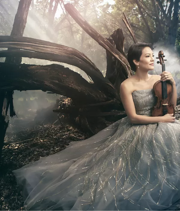 Woman in a long dress in the woods holding a violin