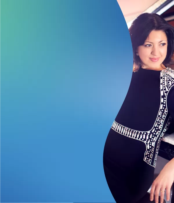 A young woman in a black dress with white trim leaning up against a  piano